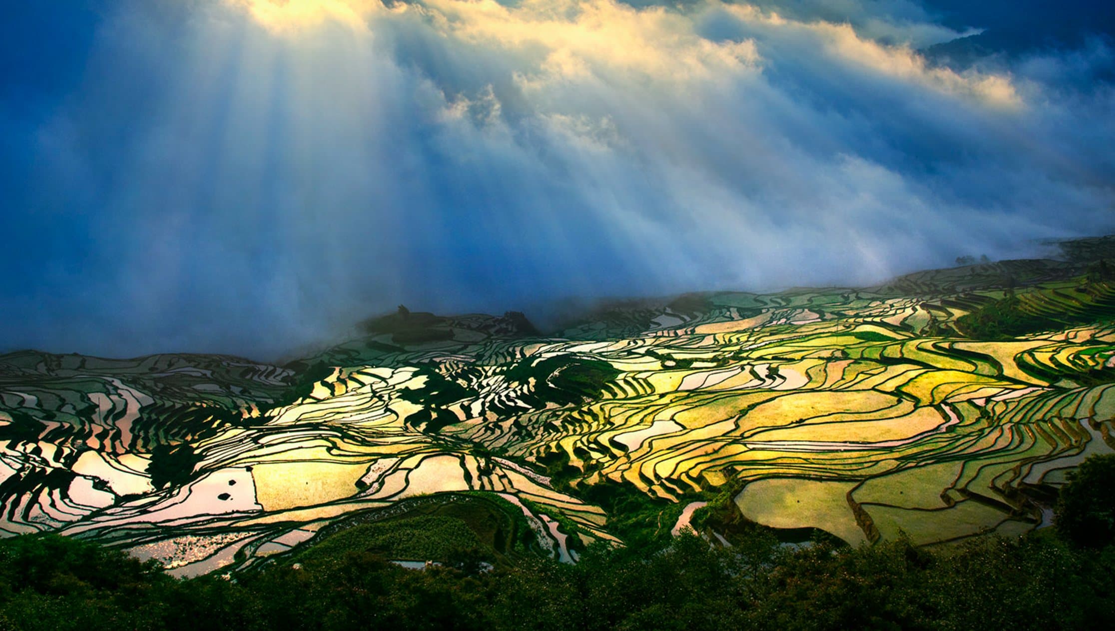 Sunlight breaking through clouds over flooded terraces